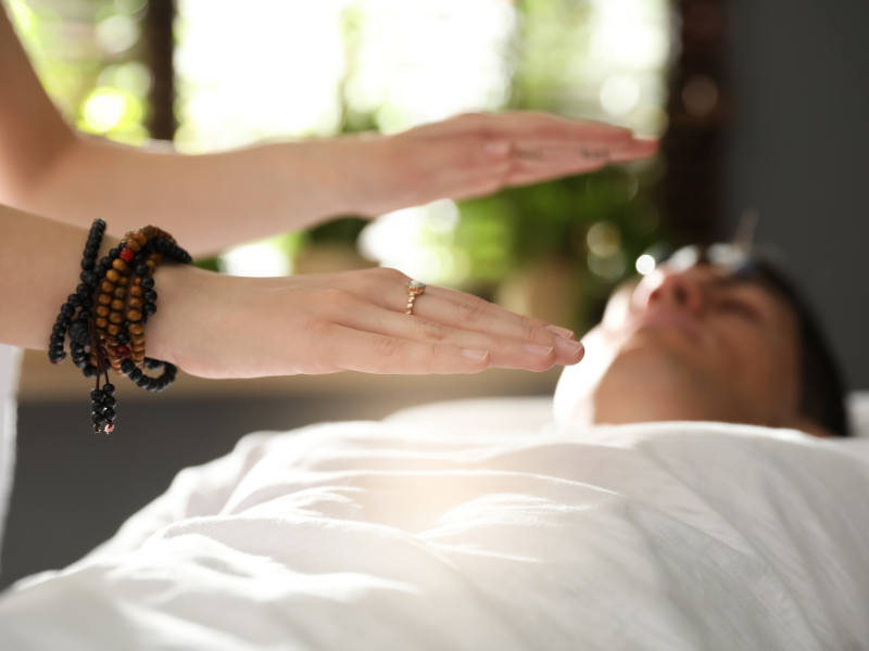 Practitioner offering Reiki healing above a resting client during a session