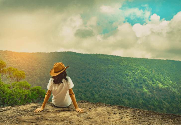 Person sitting on a mountaintop overlooking a green landscape, representing reflection, healing, and spiritual support for Simply Reiki Houston